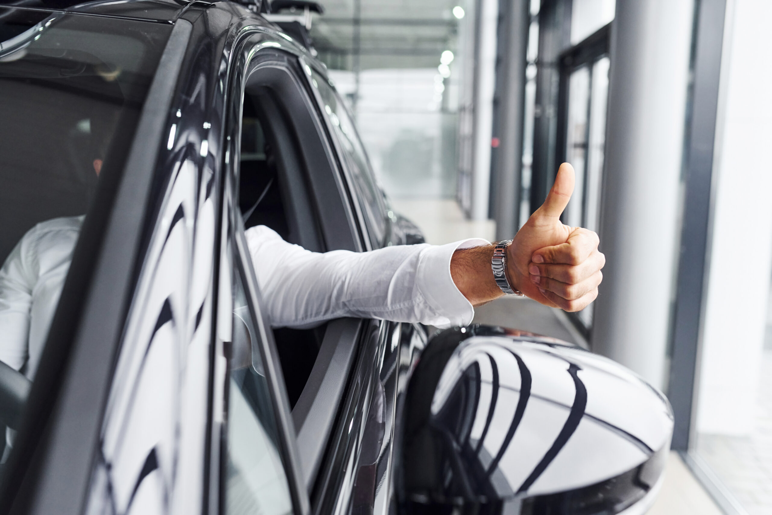 Young man in white shirt is sitting inside of a modern new automobile Young man in white shirt is sitting inside of a modern new automobile